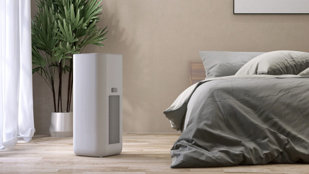 White modern design air purifier, dehumidifier in beige brown wall bedroom, gray cover sheet bed, tropical palm tree in sunlight on wood parquet floor